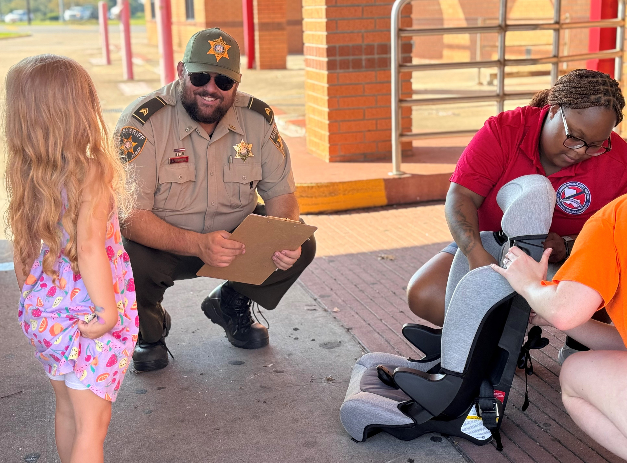 Police officer squatting to be at eye level with child. He smiles at child while two other safety workers prepare a child card set